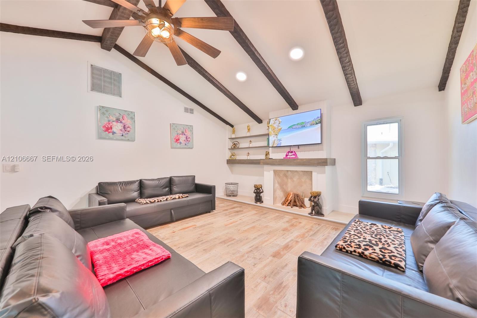 Vaulted ceiling with exposed decorative beams, wood-finish flooring, fireplace with a mantel, and built-in wall shelving
