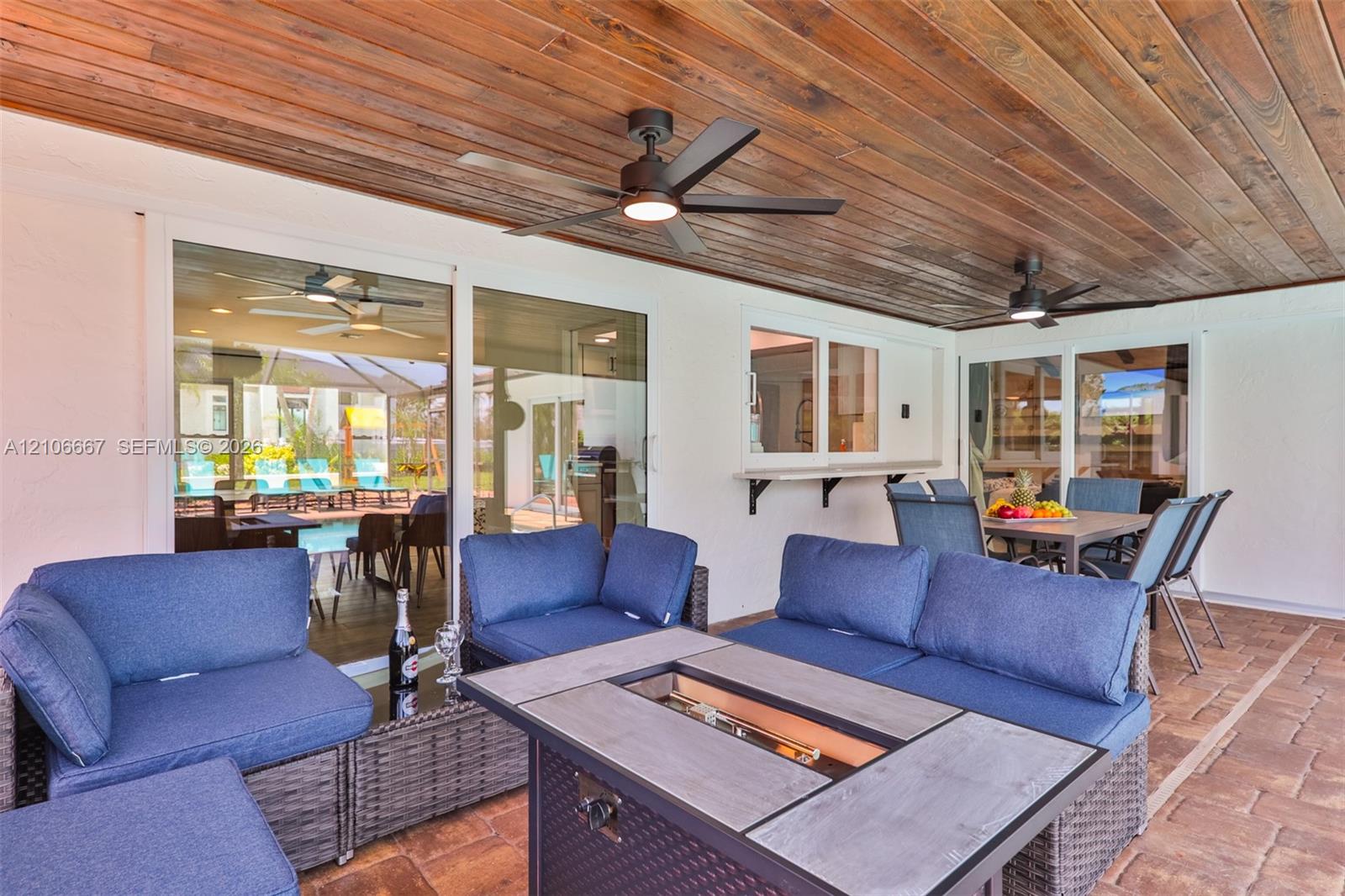 Covered outdoor patio featuring a wood-plank ceiling, paver flooring, dual ceiling fans, and an exterior pass-through window with a built-in counter