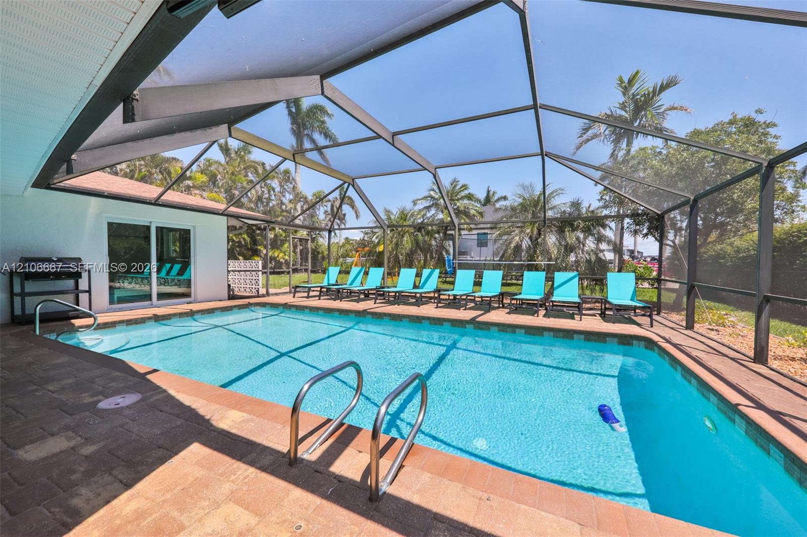 Screened-in pool enclosure featuring a paved deck, rectangular swimming pool, and metal pool ladder