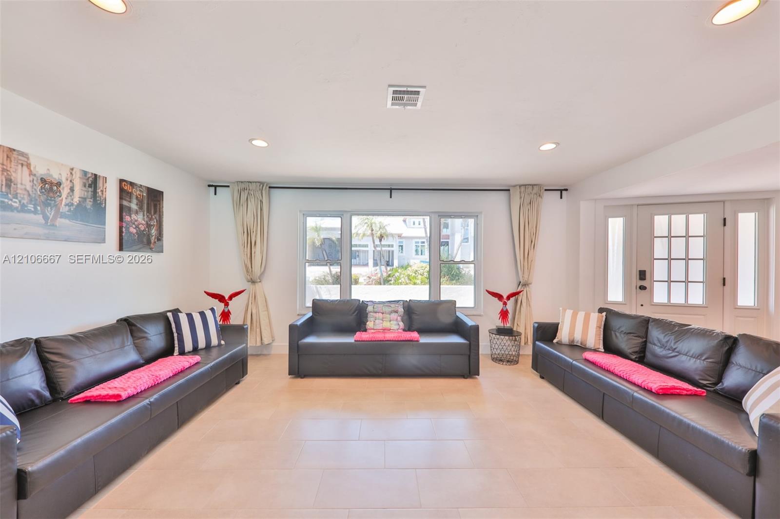Open-concept space featuring large-format tile flooring, recessed lighting, a central picture window, and a multi-pane entry door with sidelights Open-concept space featuring large-format tile flooring, recessed lighting, a central picture window, and a multi-pane entry door with sidelights