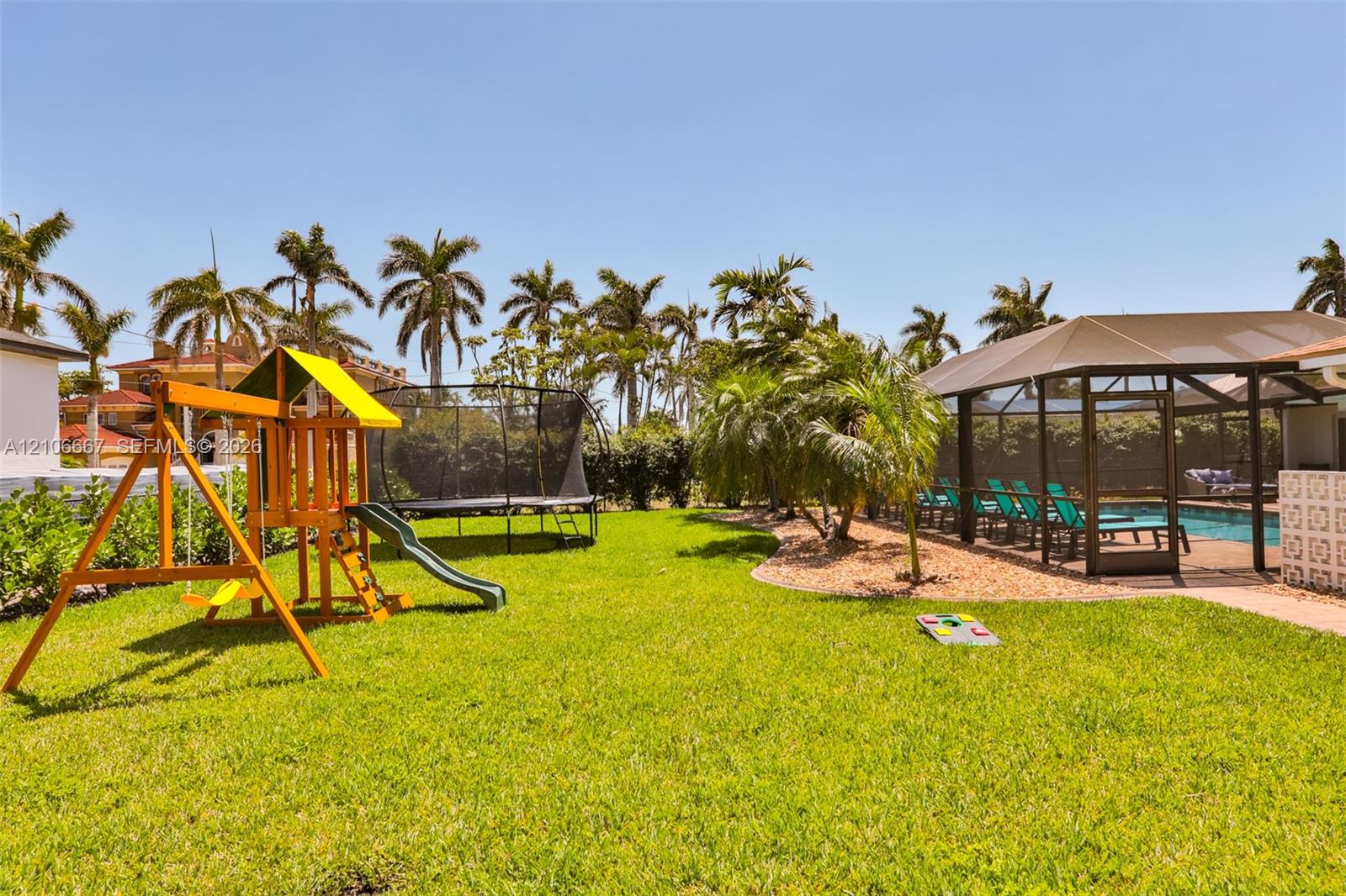 Outdoor living area featuring a screened-in swimming pool, manicured lawn, palm trees, and structural hardscaping
