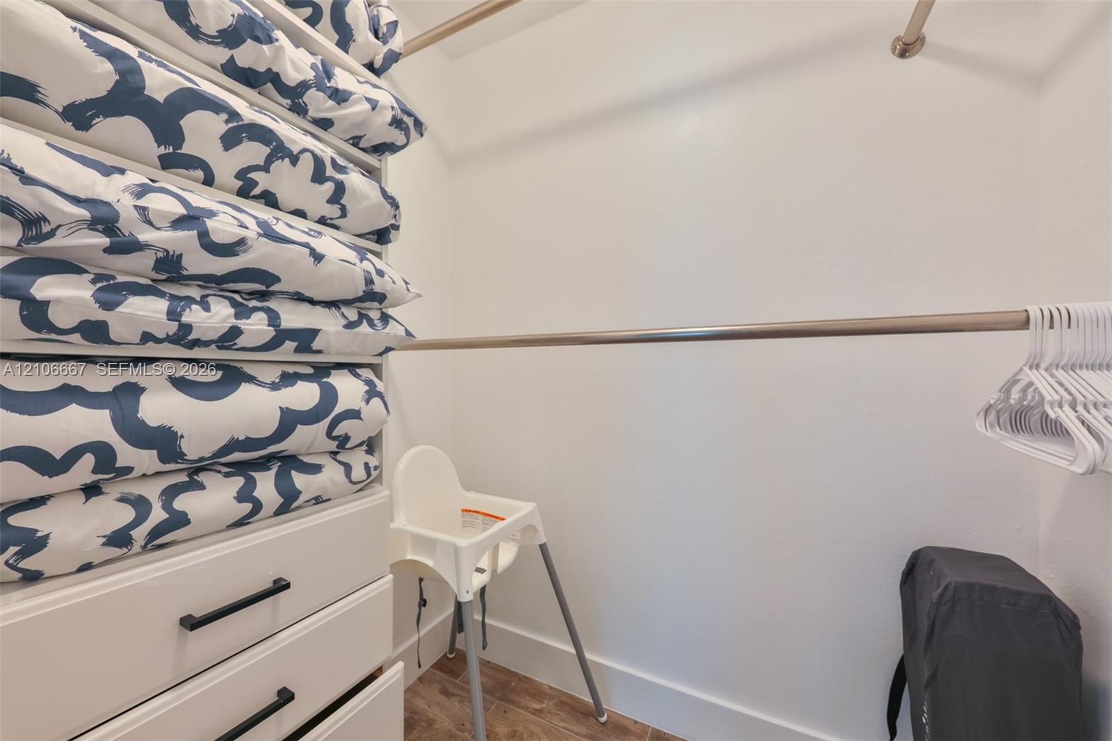 Walk-in closet featuring built-in cabinetry with matte black hardware, dual-tier metal garment rods, and wood-finish flooring