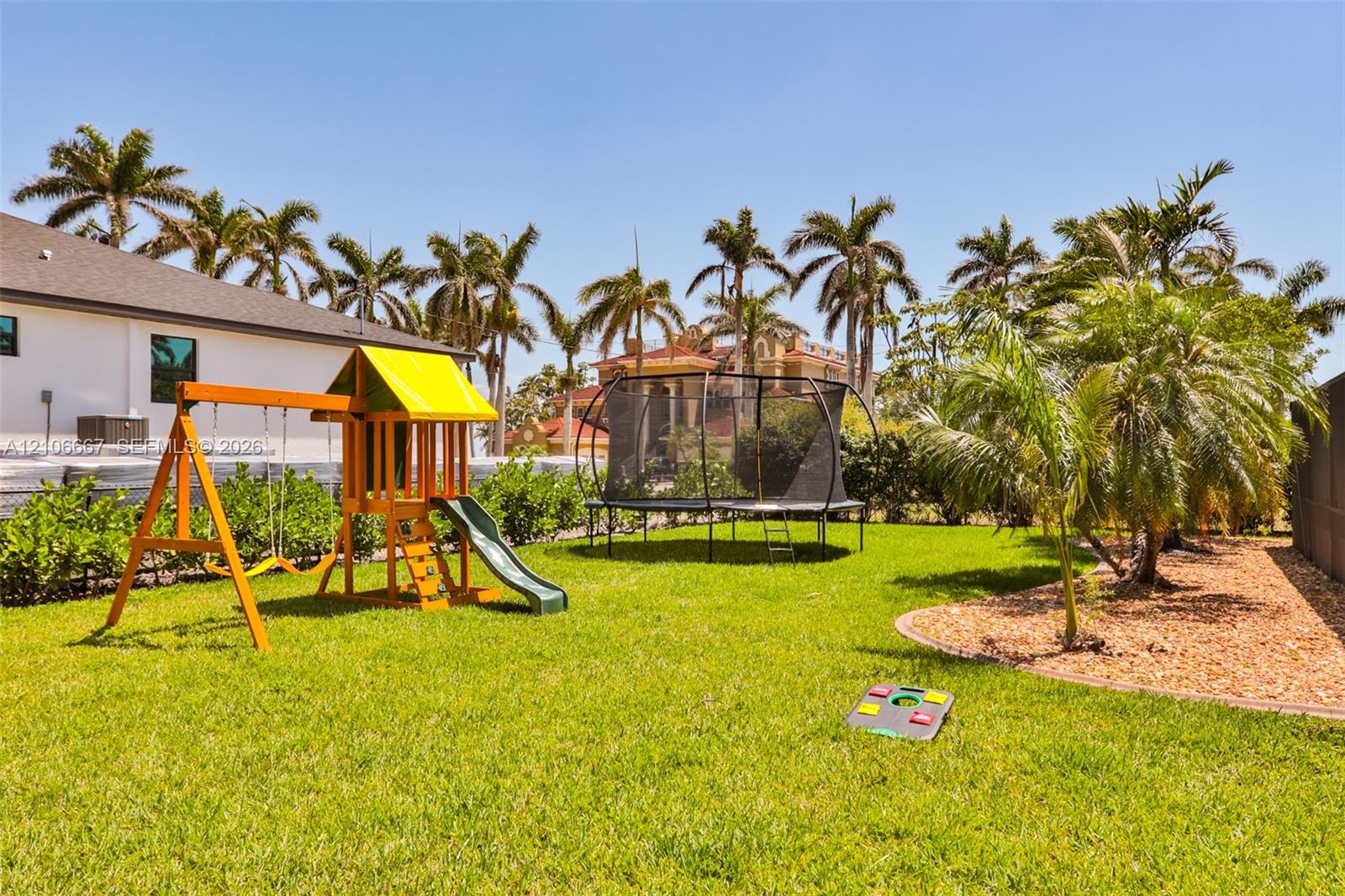 Backyard space featuring a manicured lawn, perimeter landscaping, and mature palm trees