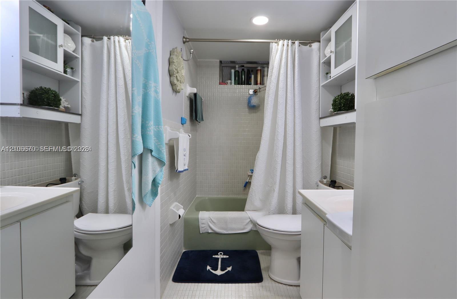 Bathroom featuring dual white cabinetry with integrated sinks, recessed ceiling lighting, a bathtub-shower combination with full-height wall tiling, and built-in upper shelving
