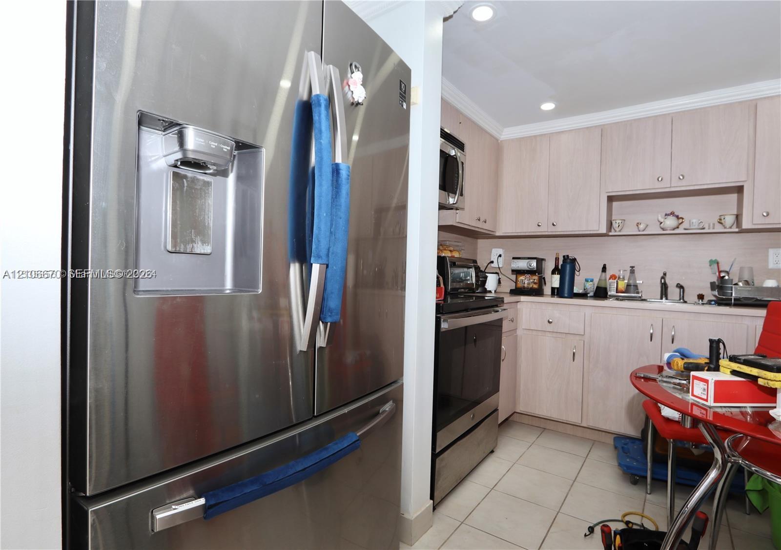 Stainless steel French-door refrigerator, light wood-finish cabinetry, recessed ceiling lighting, and ceramic tile flooring