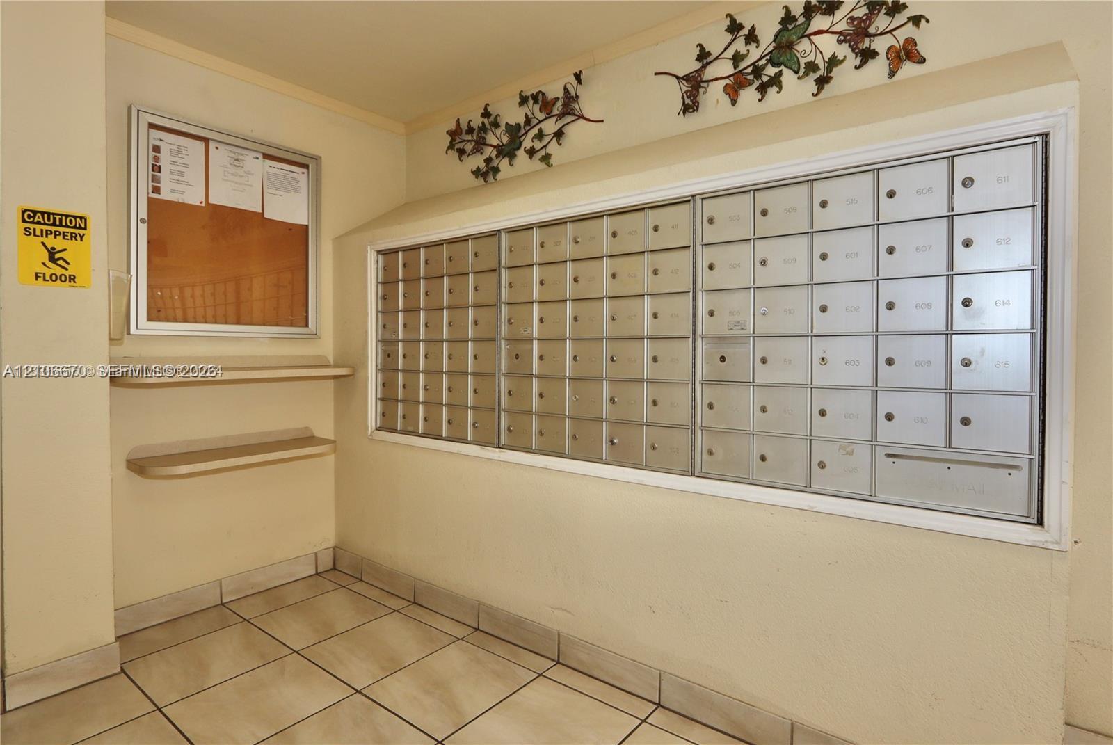 Wall-mounted metal mail distribution center, integrated bulletin board, and two recessed utility shelves with tile flooring