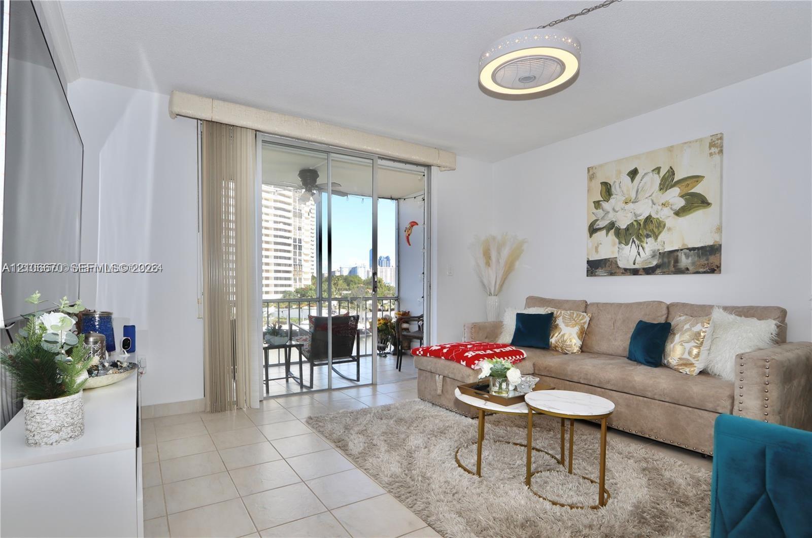 Living area featuring large-format ceramic tile flooring, a circular recessed LED ceiling light fixture, and sliding glass doors with vertical blinds