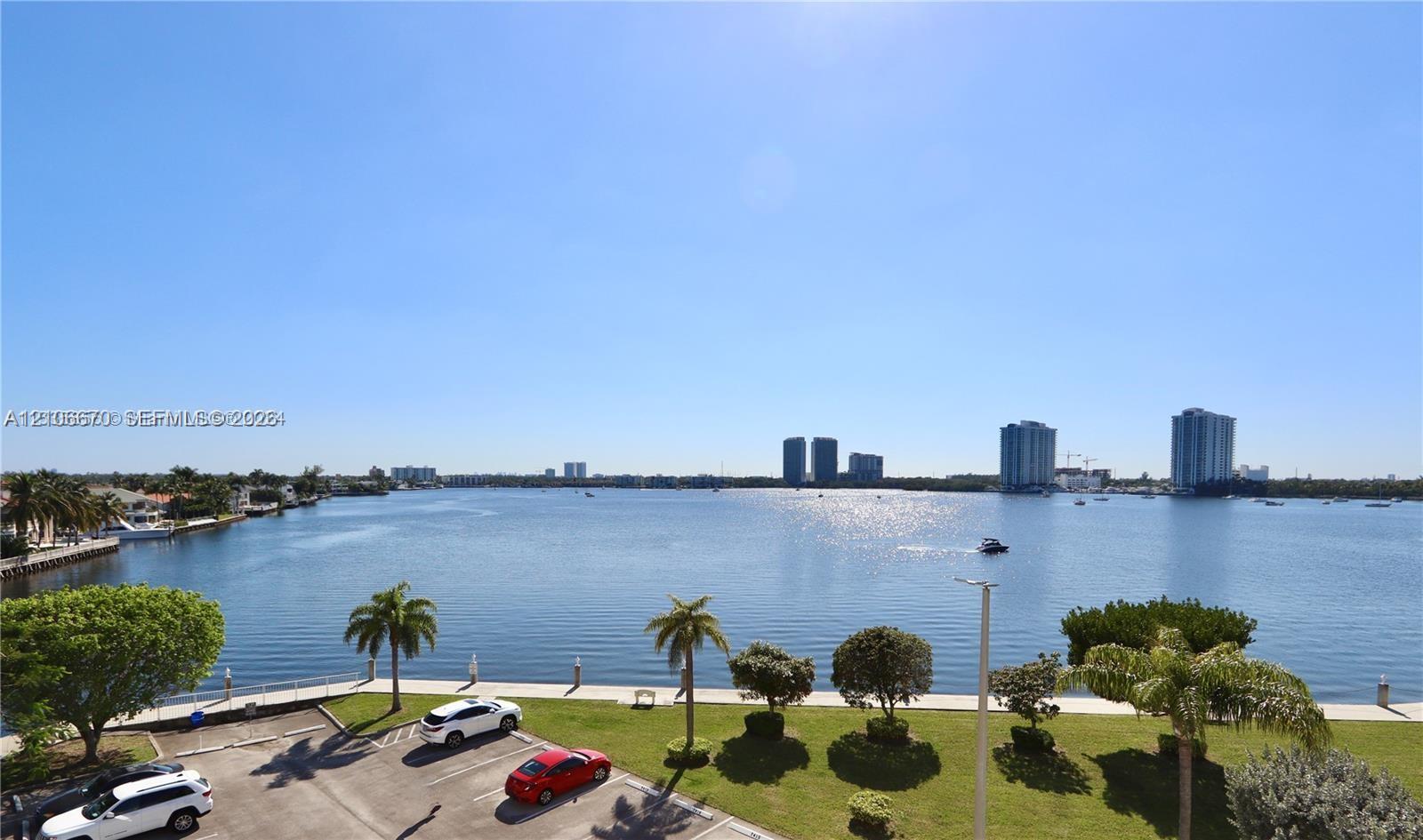 Waterfront setting featuring a bulkhead wall, landscaped lawn area, mature palm trees, and an expansive aquatic horizon