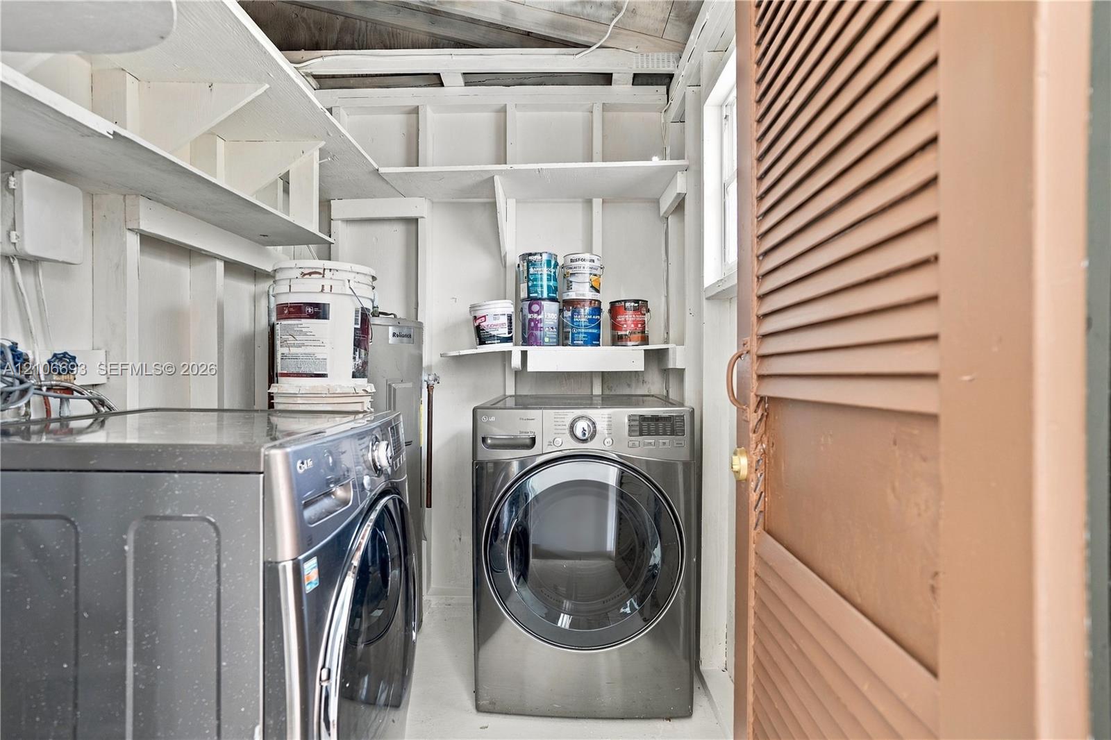 Laundry space featuring built-in open shelving, louvered door, and exposed structural framing