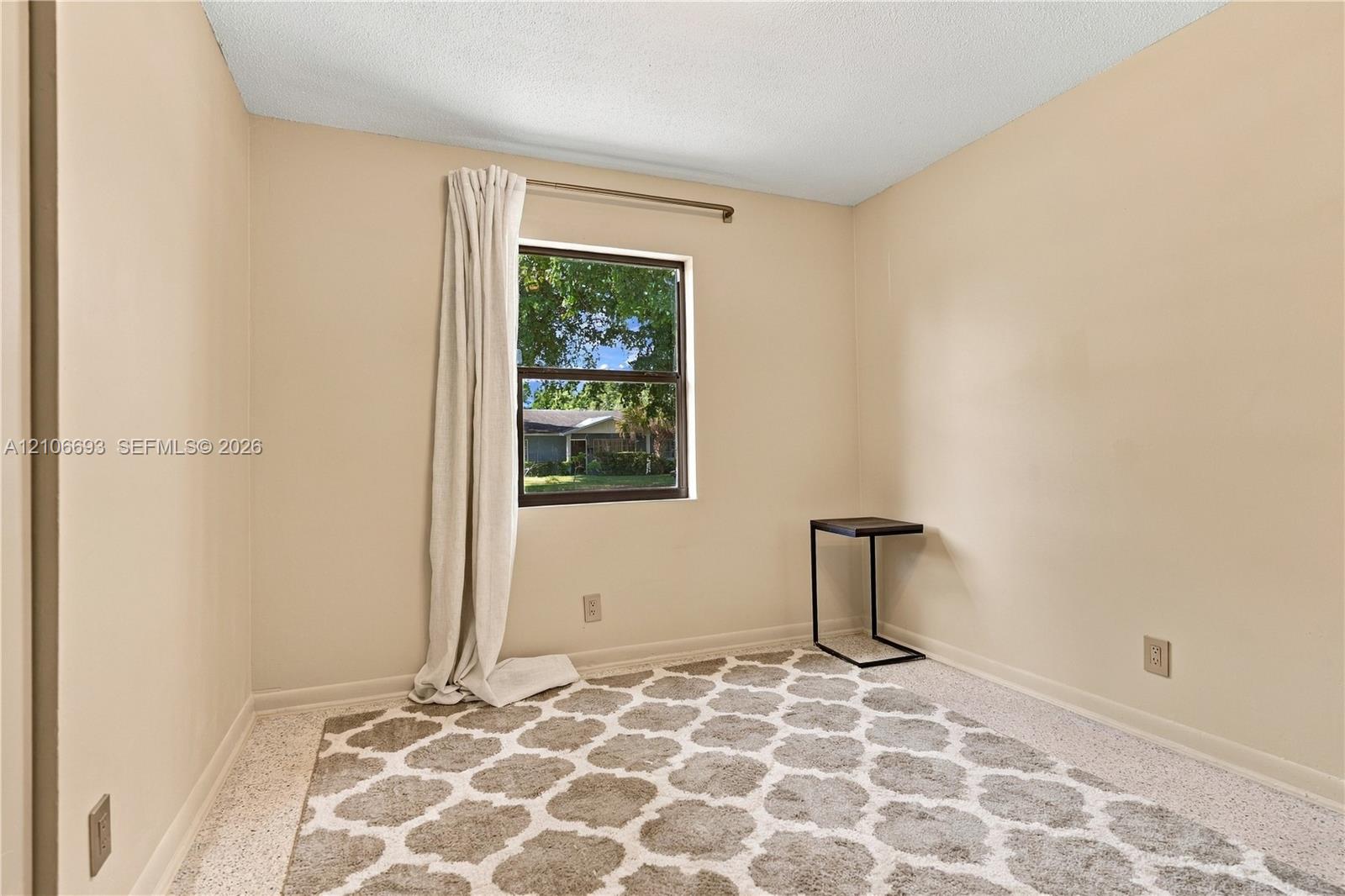 Neutral-toned room featuring a single-pane window with dark trim, textured ceiling, and terrazzo flooring Neutral-toned room featuring a single-pane window with dark trim, textured ceiling, and terrazzo flooring