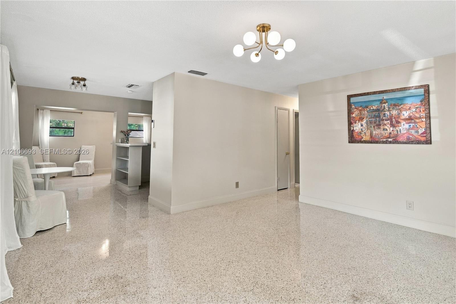 Polished stone flooring throughout, multi-arm globe chandeliers, built-in shelving unit, and neutral interior paint