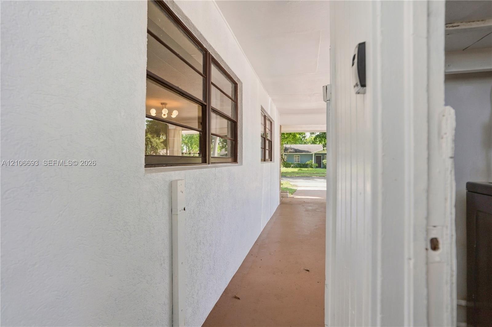 Covered exterior walkway featuring a smooth stucco finish, horizontal sliding windows with dark metal frames, and solid concrete flooring Covered exterior walkway featuring a smooth stucco finish, horizontal sliding windows with dark metal frames, and solid concrete flooring