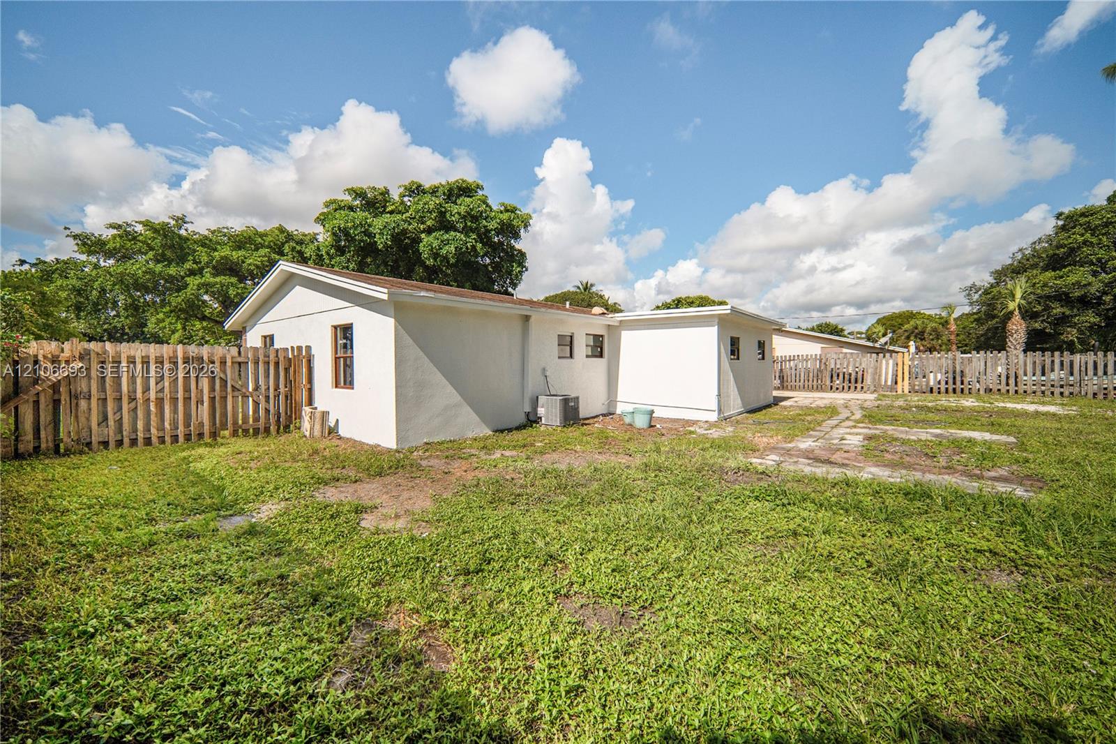 Exterior rear elevation featuring a stucco finish, gable roofline, wood privacy fencing, and an expansive lawn Exterior rear elevation featuring a stucco finish, gable roofline, wood privacy fencing, and an expansive lawn