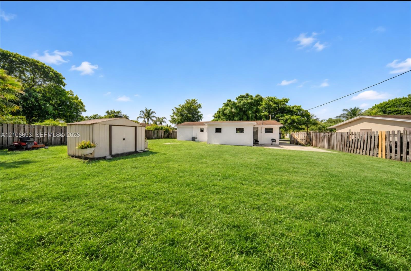 Expansive backyard featuring a large grass lawn, perimeter wood fencing, and a detached storage shed