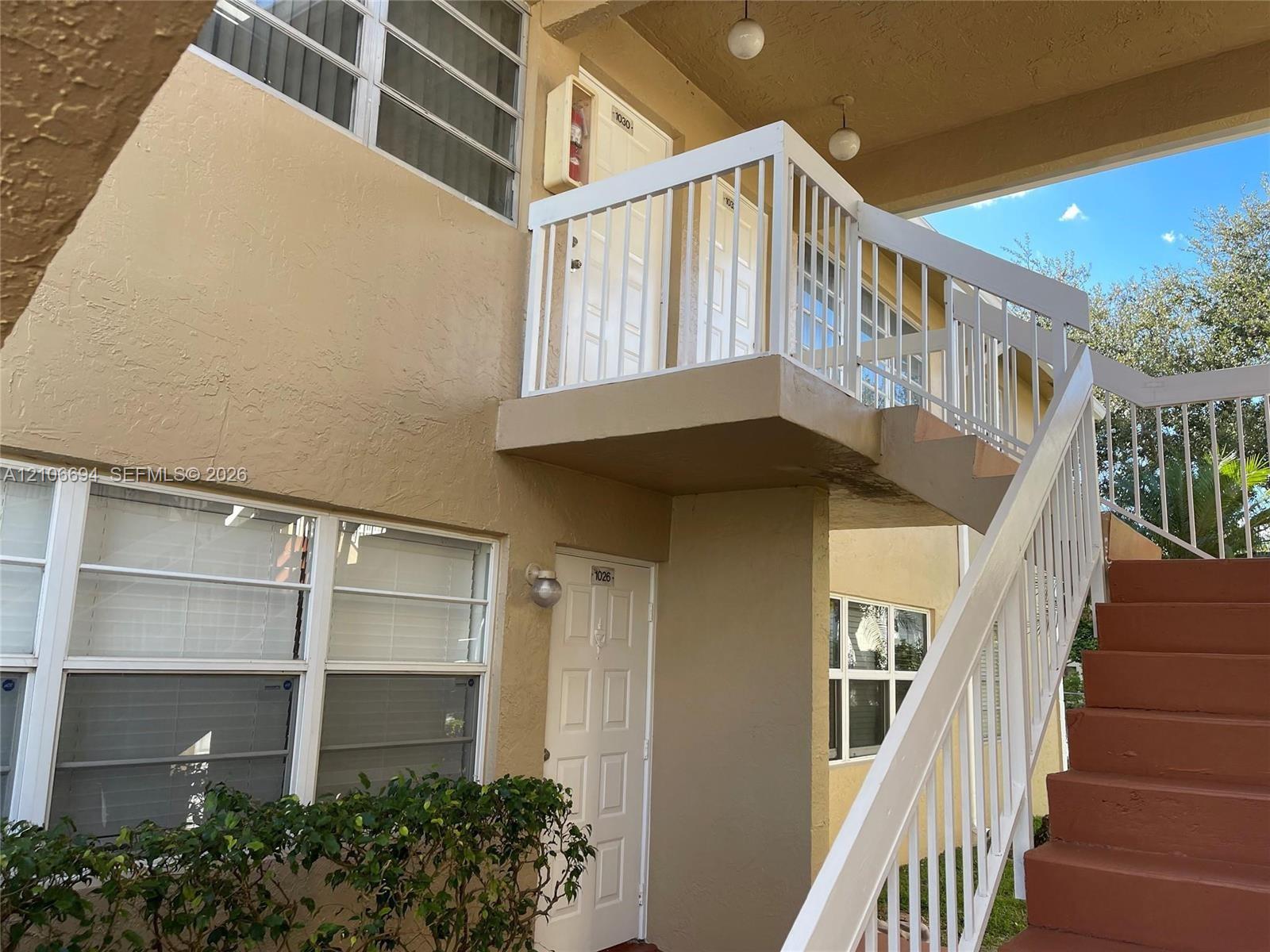 Exterior facade featuring a covered entryway, white metal railing, and staircase