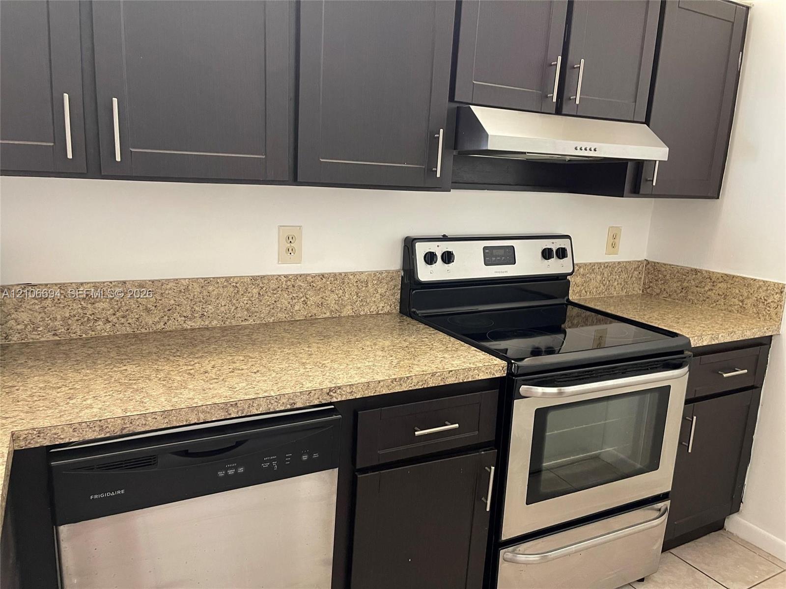 Dark cabinetry featuring brushed metal hardware, stone-finish countertops, stainless steel electric range, stainless steel dishwasher, and mounted stainless steel vent hood