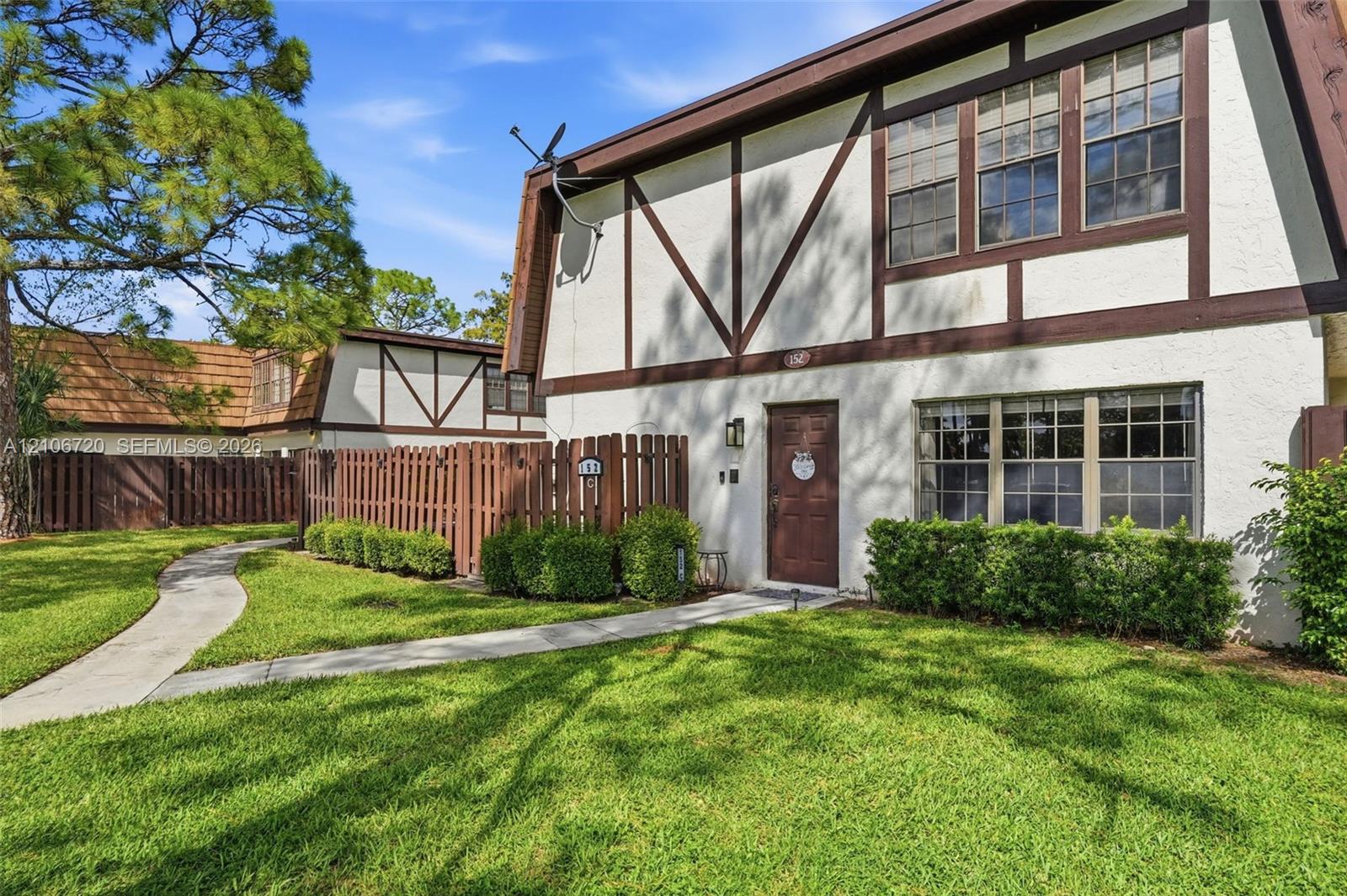 Tudor-style exterior featuring stucco facade with timber framing, multi-pane windows, a private fenced entry courtyard, and mature landscaping Tudor-style exterior featuring stucco facade with timber framing, multi-pane windows, a private fenced entry courtyard, and mature landscaping