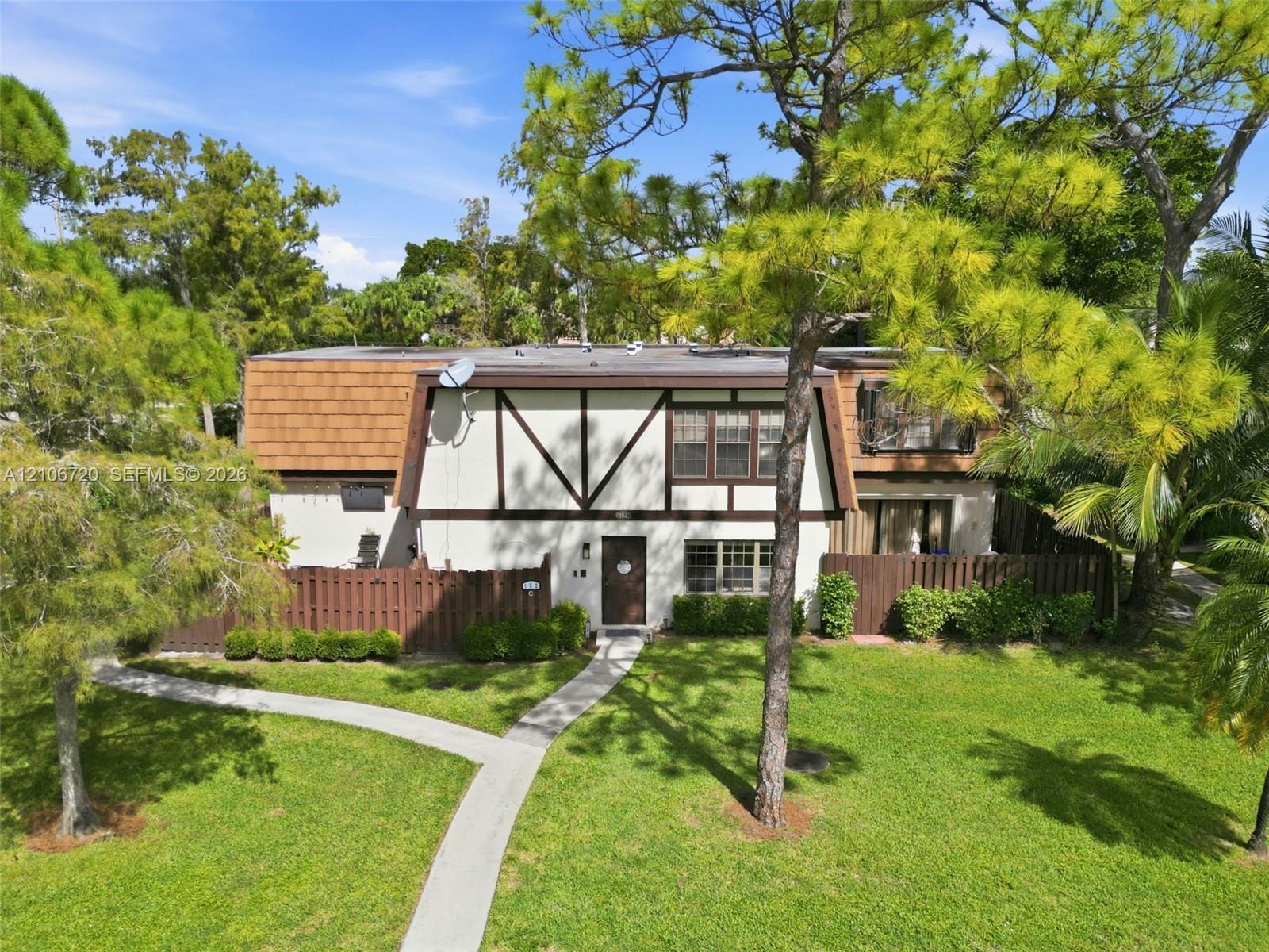 Mansard-style exterior featuring half-timbered detailing, a paved walkway, and an enclosed privacy fence