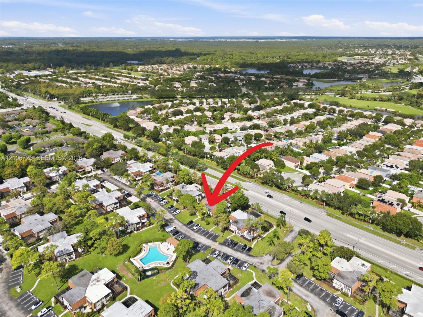Aerial perspective of a multi-unit residential community featuring mature landscaping and a centrally located outdoor swimming pool