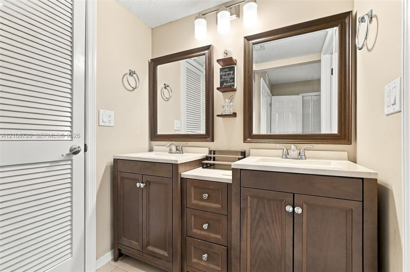 Double vanity featuring wood cabinetry, stone-composite countertops with integrated sinks, three-light overhead fixture, and dual framed mirrors