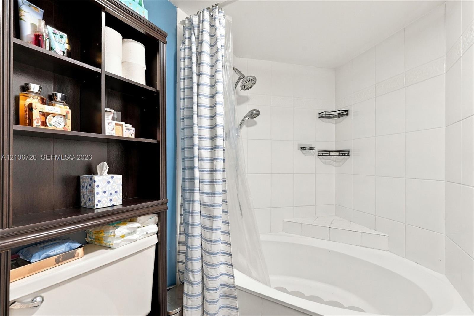 Built-in floor-to-ceiling shelving, soaking tub with integrated corner seating, and white tile tub surround featuring dual shower heads and metal wall-mounted storage racks