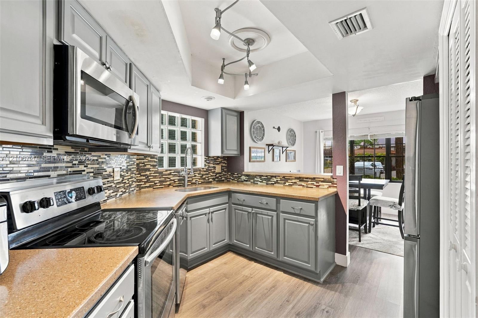 Kitchen featuring gray cabinetry, composite countertops, multi-toned tile backsplash, stainless steel appliances, and wood-finish flooring