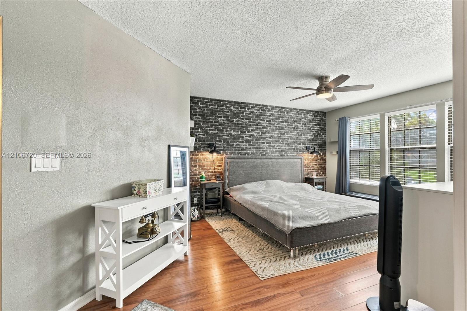 Bedroom featuring wood-finish flooring, a textured accent wall, integrated wall-mounted lighting, and a ceiling fan