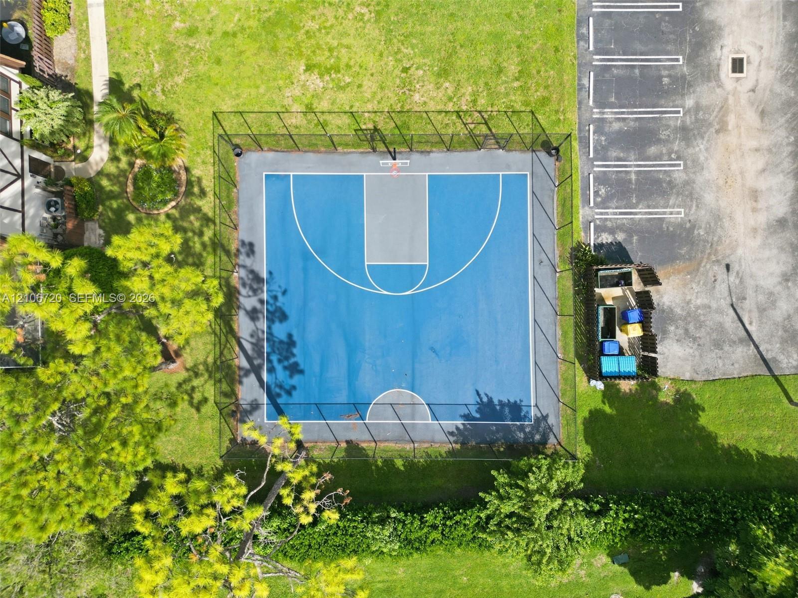 Fenced basketball court featuring a multi-tone blue hard surface, permanent hoop assembly, and perimeter chain-link enclosure