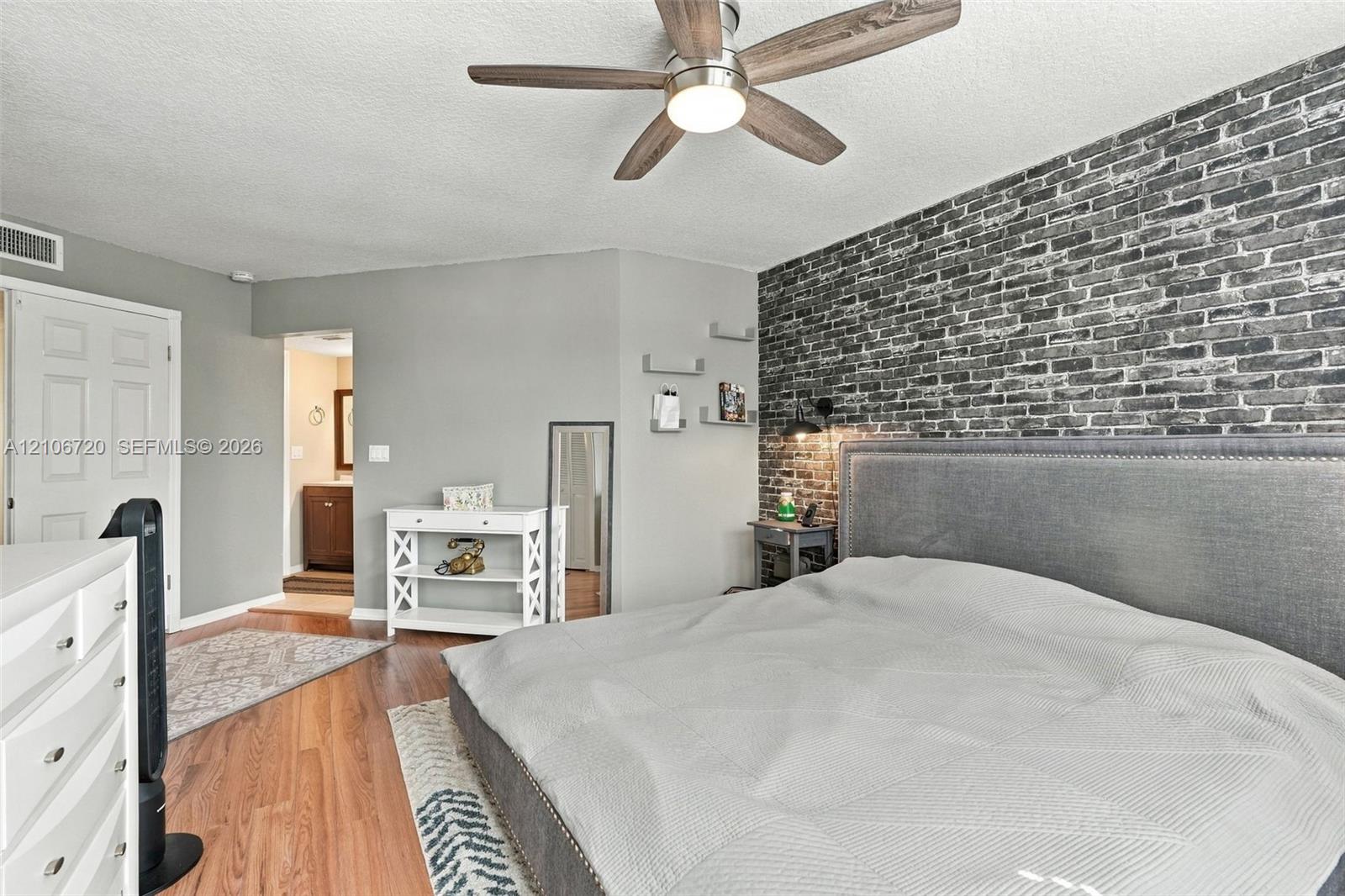 Bedroom featuring an exposed brick accent wall, wood-finish flooring, and a ceiling fan with integrated lighting