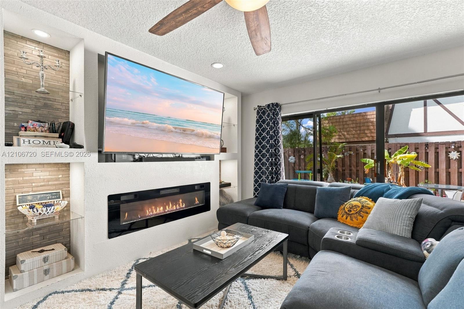 Built-in wall cabinetry with recessed lighting, stone-tiled accent shelving, linear electric fireplace, and sliding glass patio doors