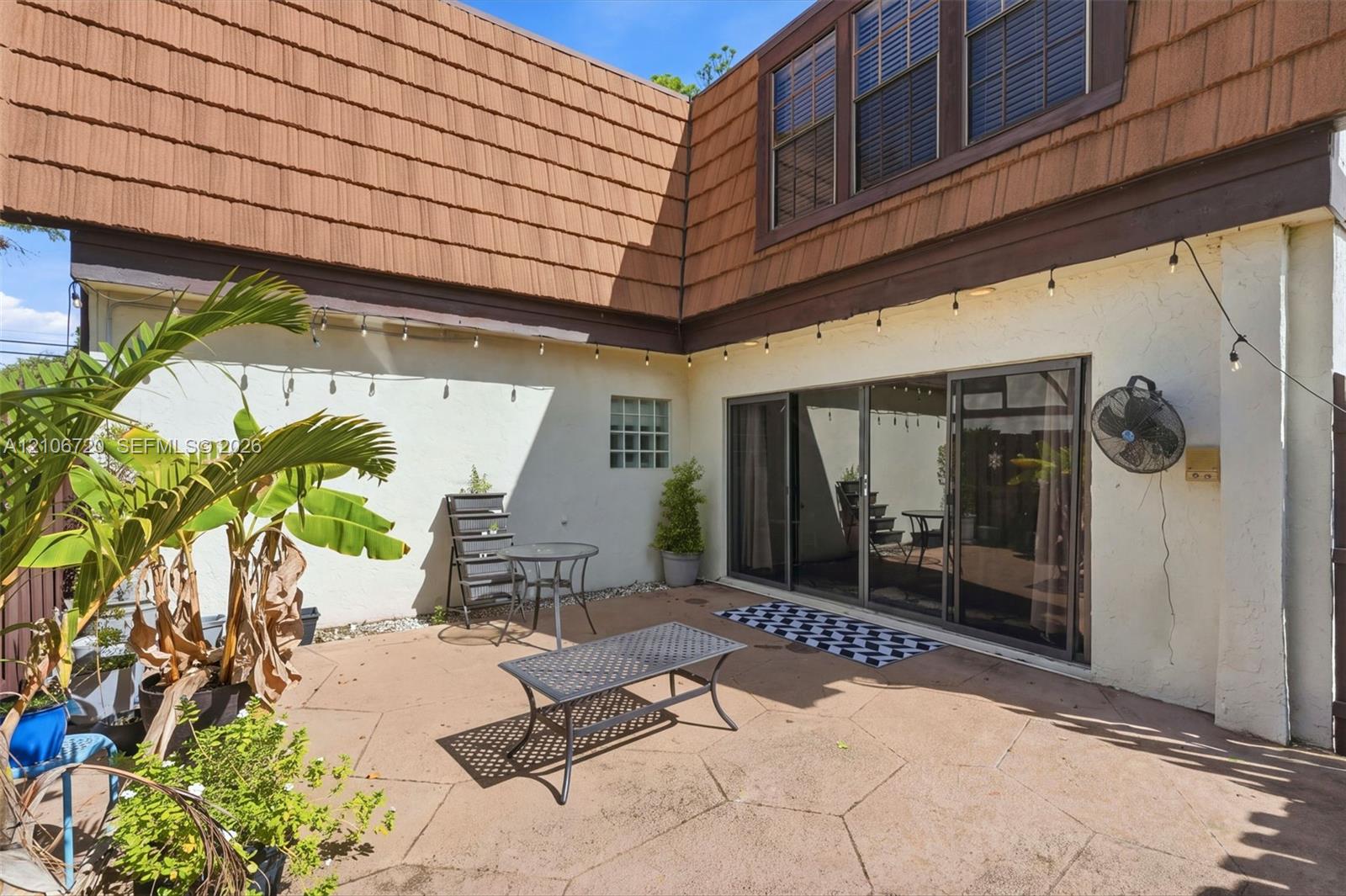 Concrete paver patio featuring stucco exterior walls, sliding glass doors, glass block accent window, and brown shake siding