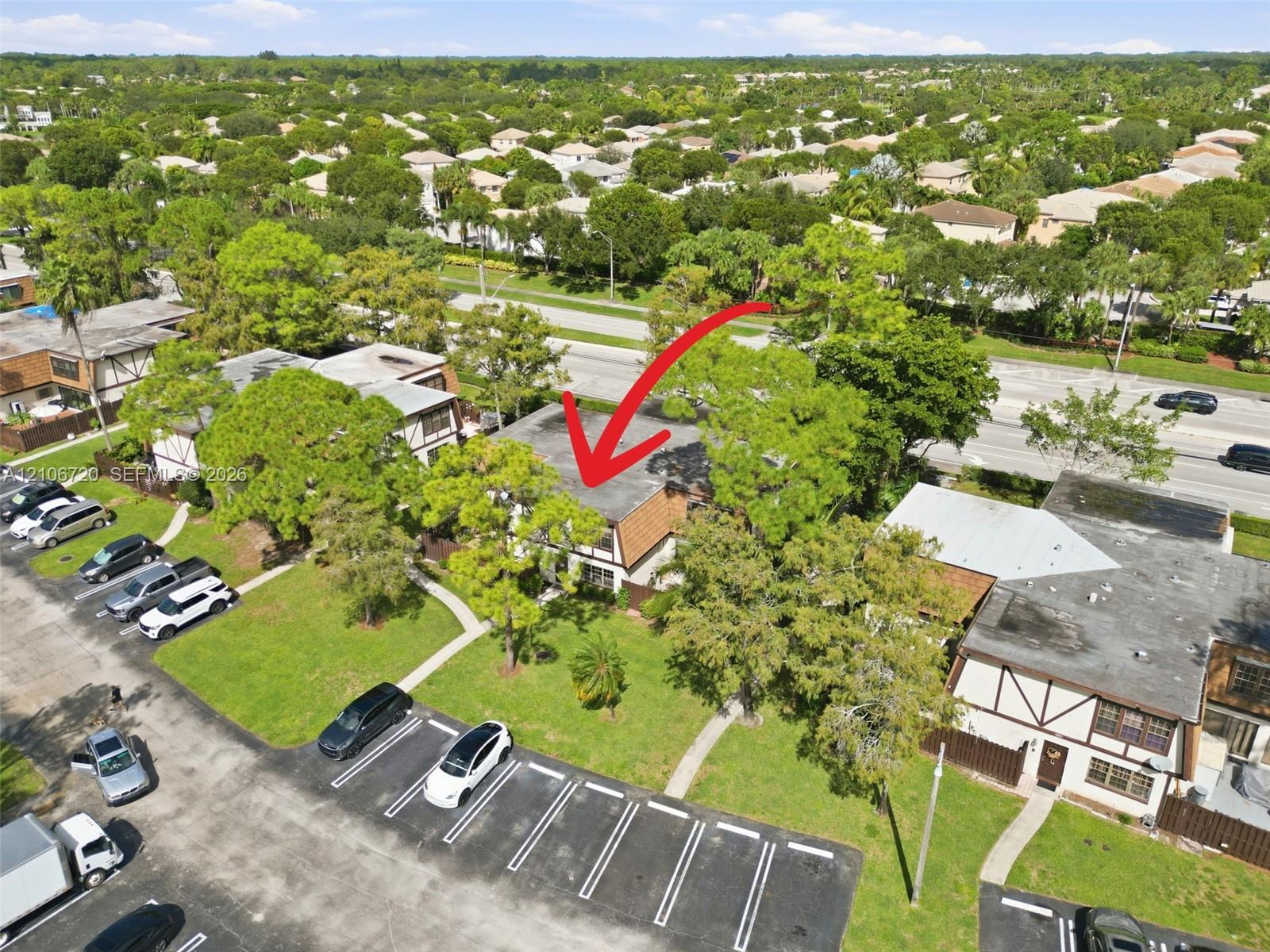 Aerial perspective of a multi-unit complex featuring shingled rooflines, exterior timber-frame detailing, established shade trees, and dedicated asphalt parking areas