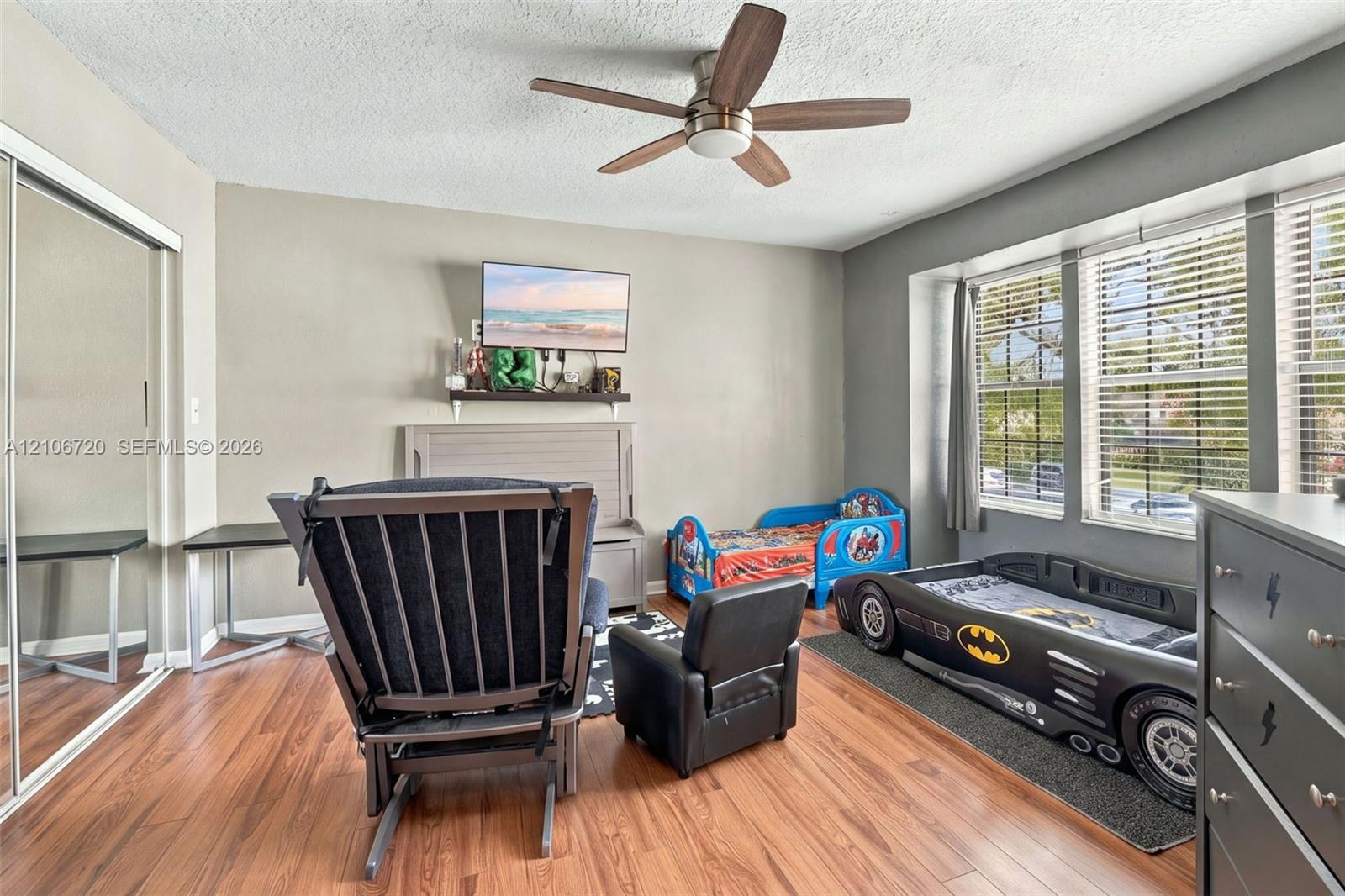 Wood-finish flooring, ceiling fan with integrated lighting, mirrored sliding-door closet, and large multi-pane windows with horizontal blinds