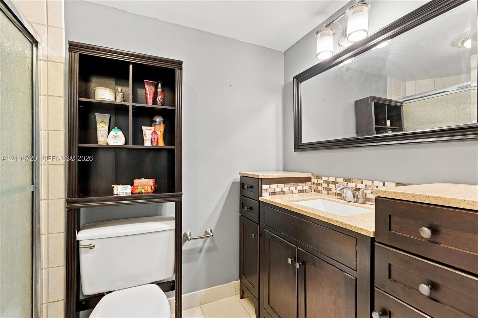 Dark wood vanity with a stone-finish countertop, integrated undermount sink, multi-tile backsplash, and expansive framed wall mirror with overhead multi-light fixture