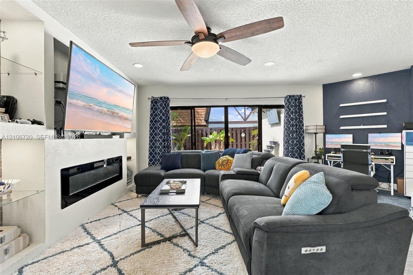 Living area featuring a recessed fireplace with built-in shelving, a centrally mounted ceiling fan, recessed lighting, and expansive floor-to-ceiling glass sliding doors