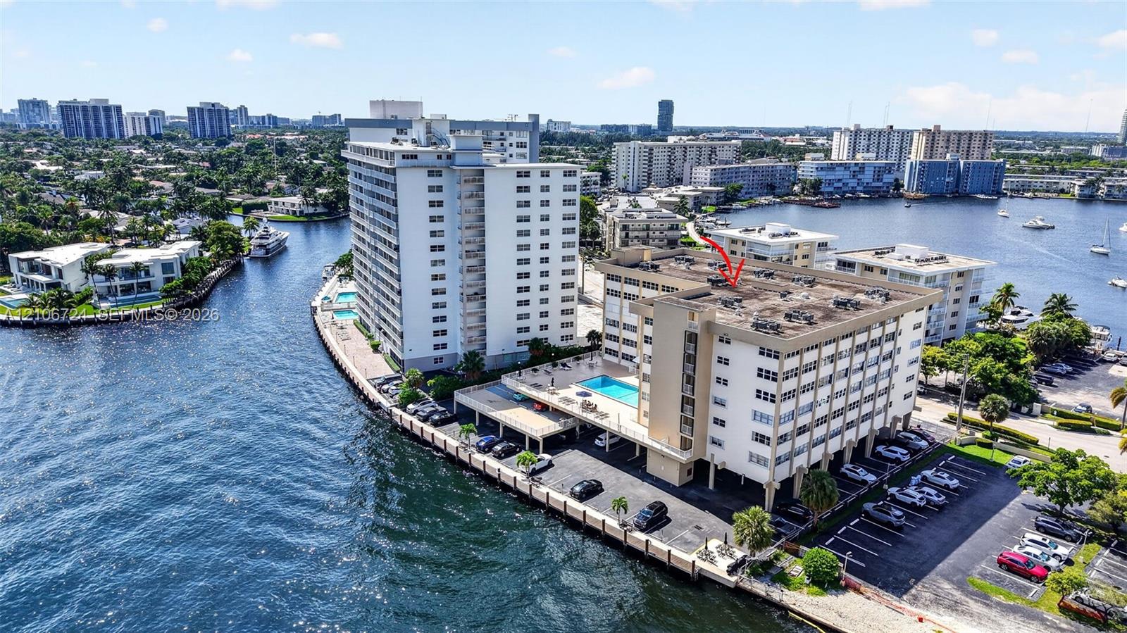 Aerial perspective of waterfront mid-rise building featuring a swimming pool, covered parking, and direct maritime waterway access