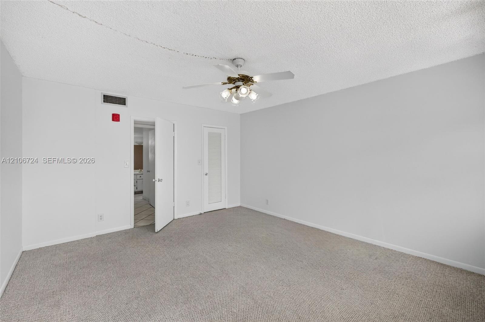 Neutral-toned carpeted flooring, textured ceiling, and four-blade ceiling fan with integrated multi-bulb light fixture