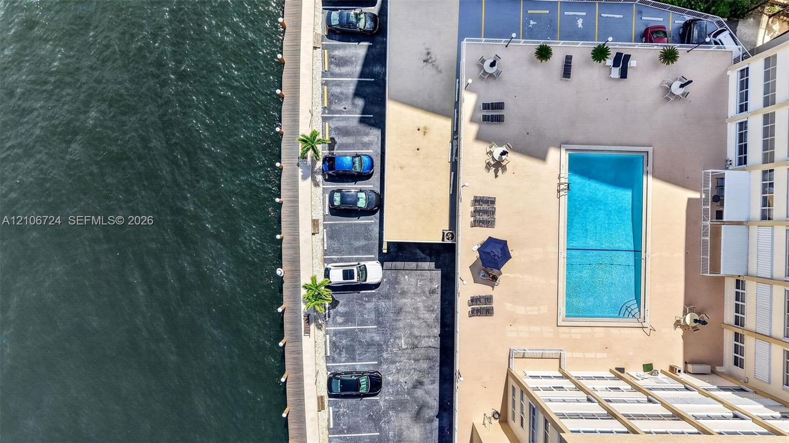 Waterfront property featuring a rectangular swimming pool, concrete pool deck, and on-site parking area