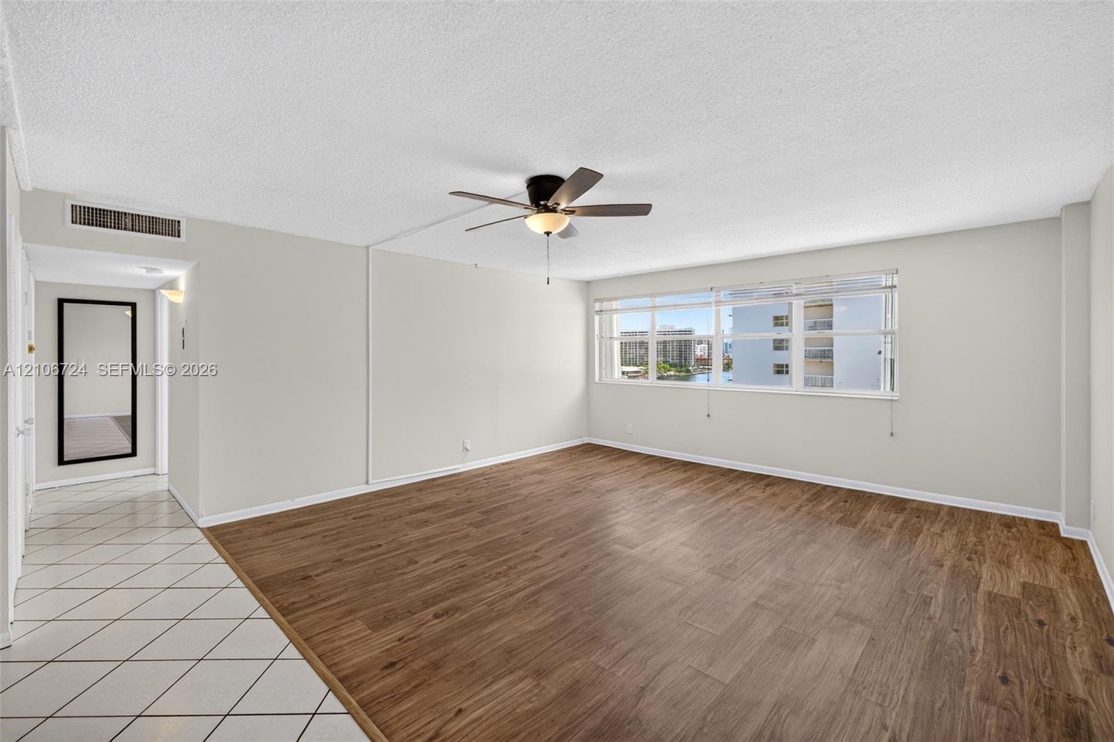 Open-concept living space featuring wood-finish flooring, white tile entryway, multi-pane windows, and a central ceiling fan with integrated lighting