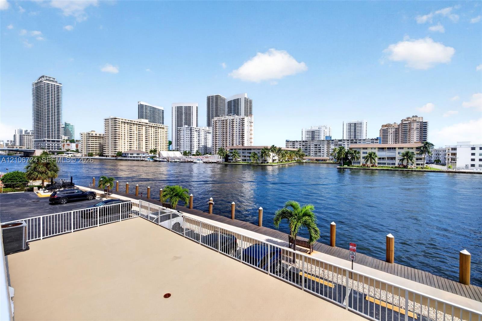 Elevated outdoor terrace featuring a white metal railing, paved surface, and direct water frontage with a private dock