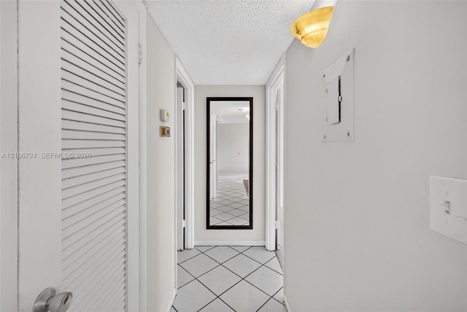 Hallway featuring diamond-patterned tile flooring, louvered closet door, and half-dome wall-mounted light fixture