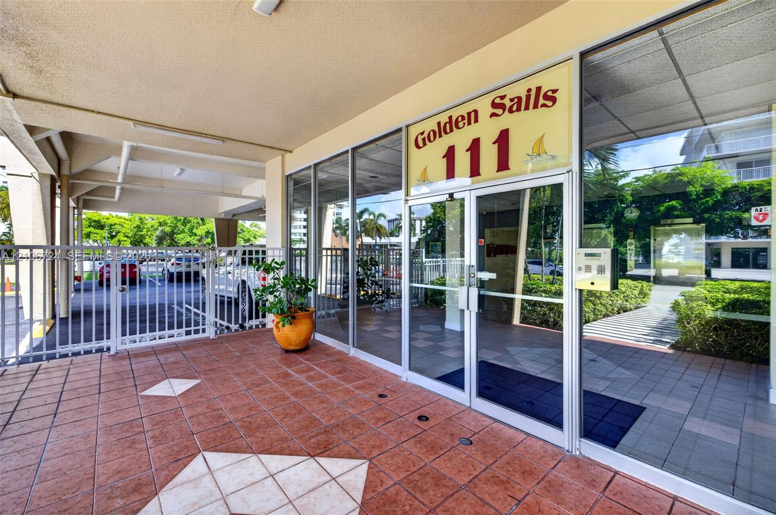 Covered entryway featuring terra cotta tile flooring, expansive floor-to-ceiling glass windows, secured metal gate access, and built-in intercom system