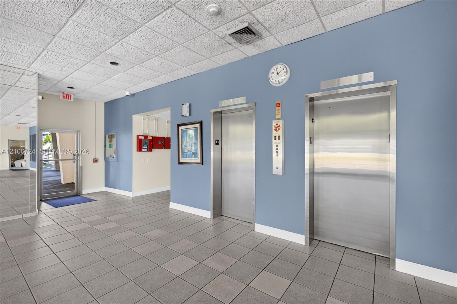 Lobby area featuring dual stainless steel elevators, ceramic tile flooring, and mirrored wall paneling