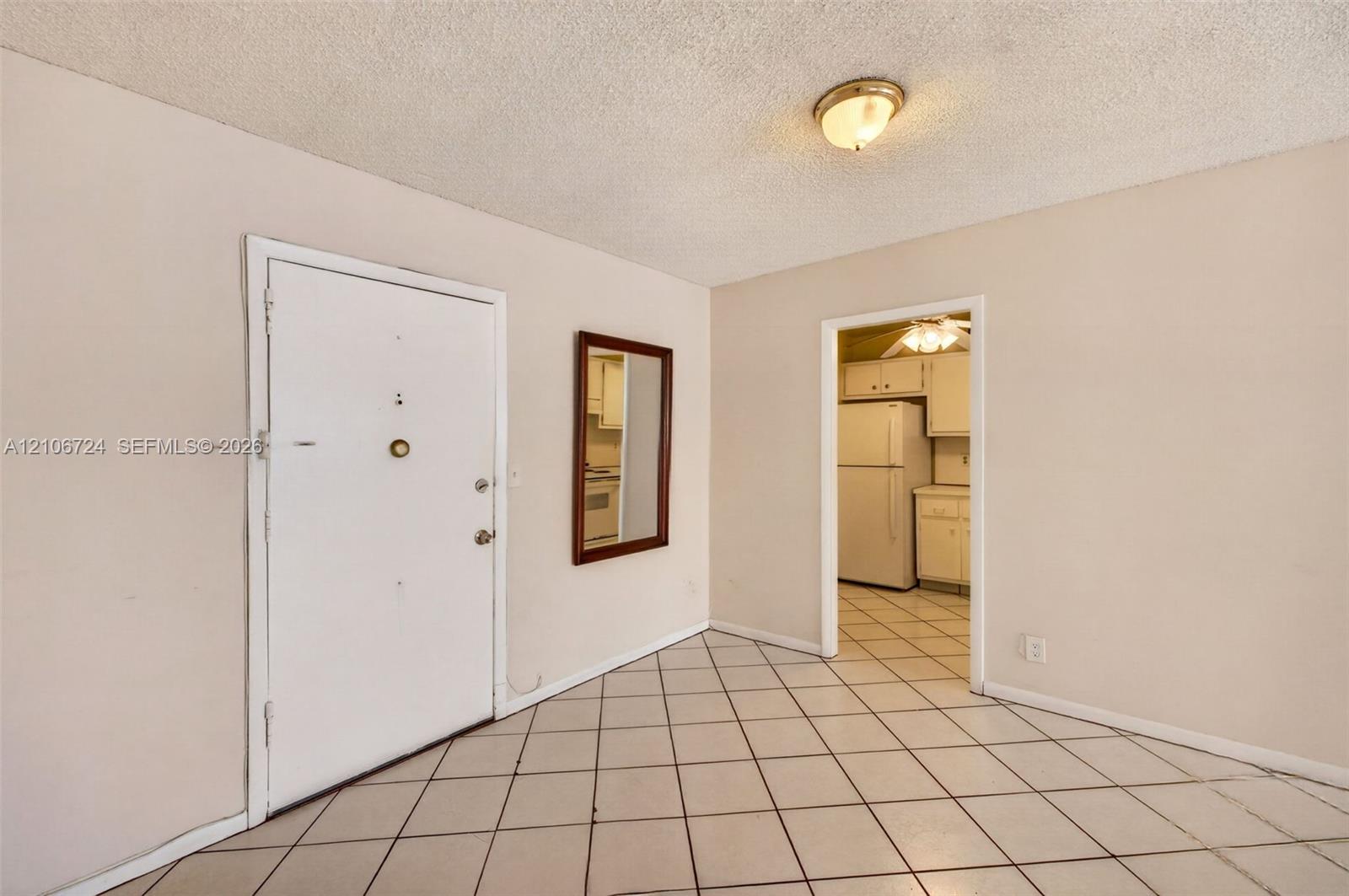 Ceramic tile flooring arranged in a diagonal pattern, textured ceiling with a dome-style flush-mount light fixture, and an entry door with integrated hardware