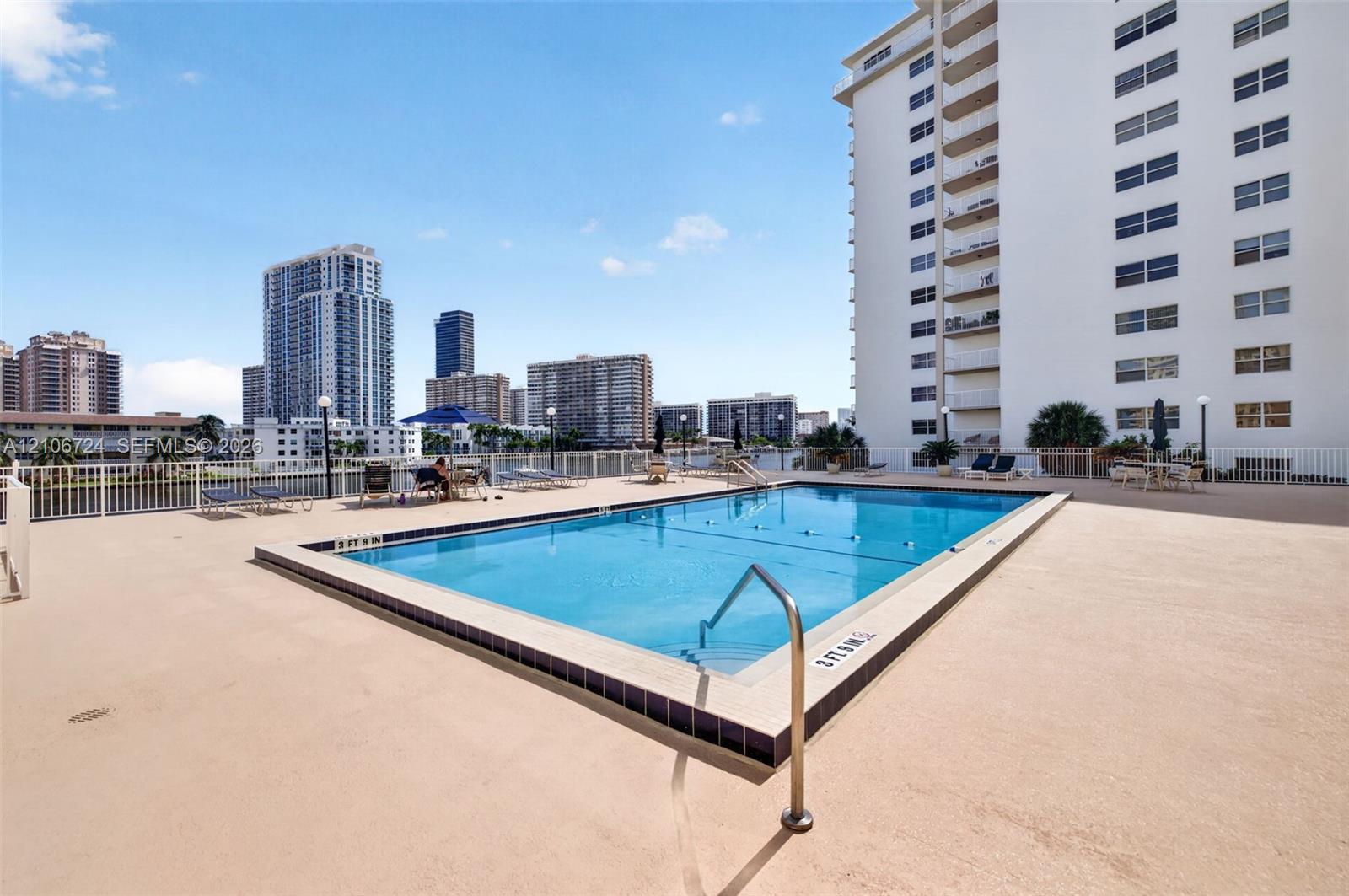 Rectangular outdoor swimming pool featuring a tiled waterline, metal handrails, and a surrounding paved deck