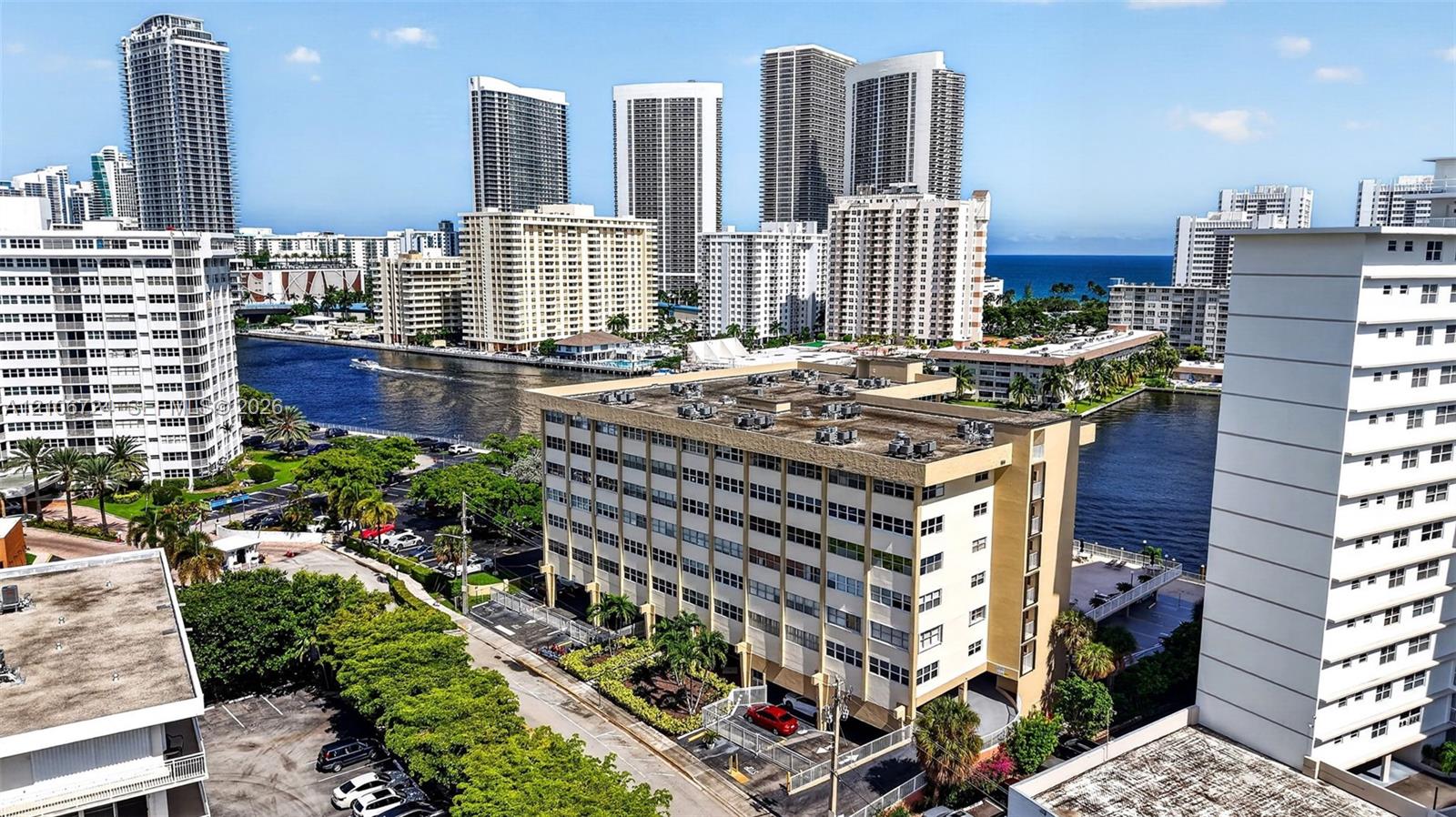 Mid-rise multi-story building featuring a concrete facade, flat roof with roof-mounted HVAC units, ground-level covered parking, and an urban waterfront location