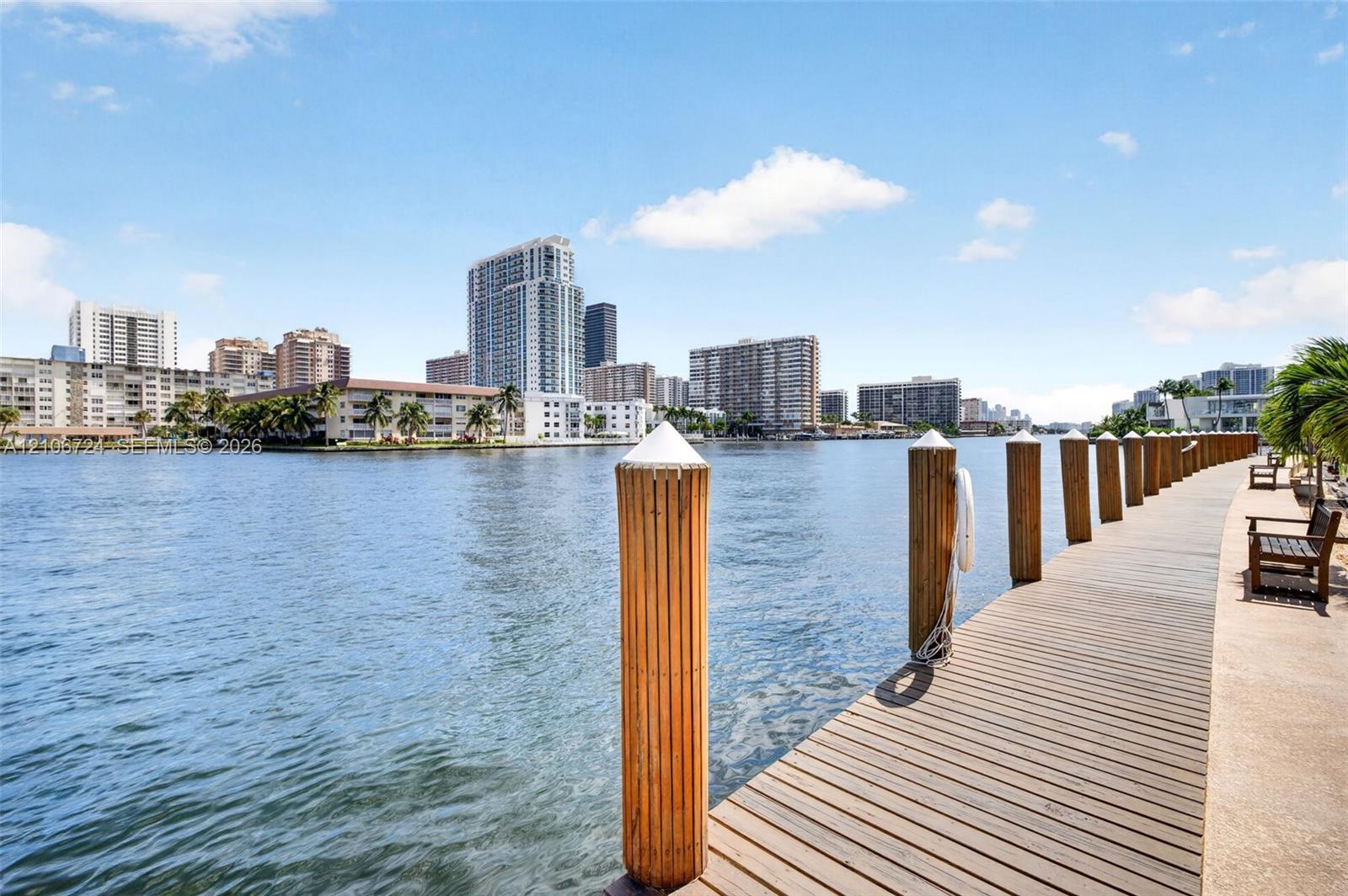 Waterfront wooden dock featuring rounded pilings and a concrete walkway
