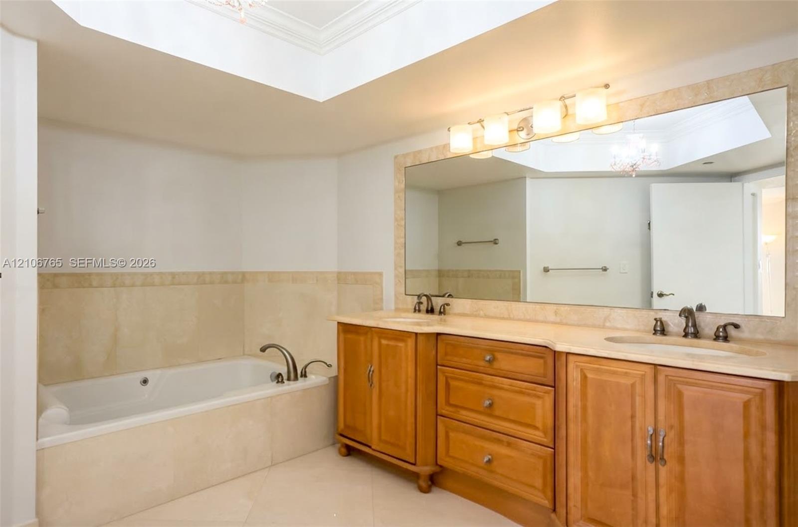 Main bathroom, soaking tub with stone tile surround, dual-sink vanity with wood cabinetry, and large wall-mounted mirror