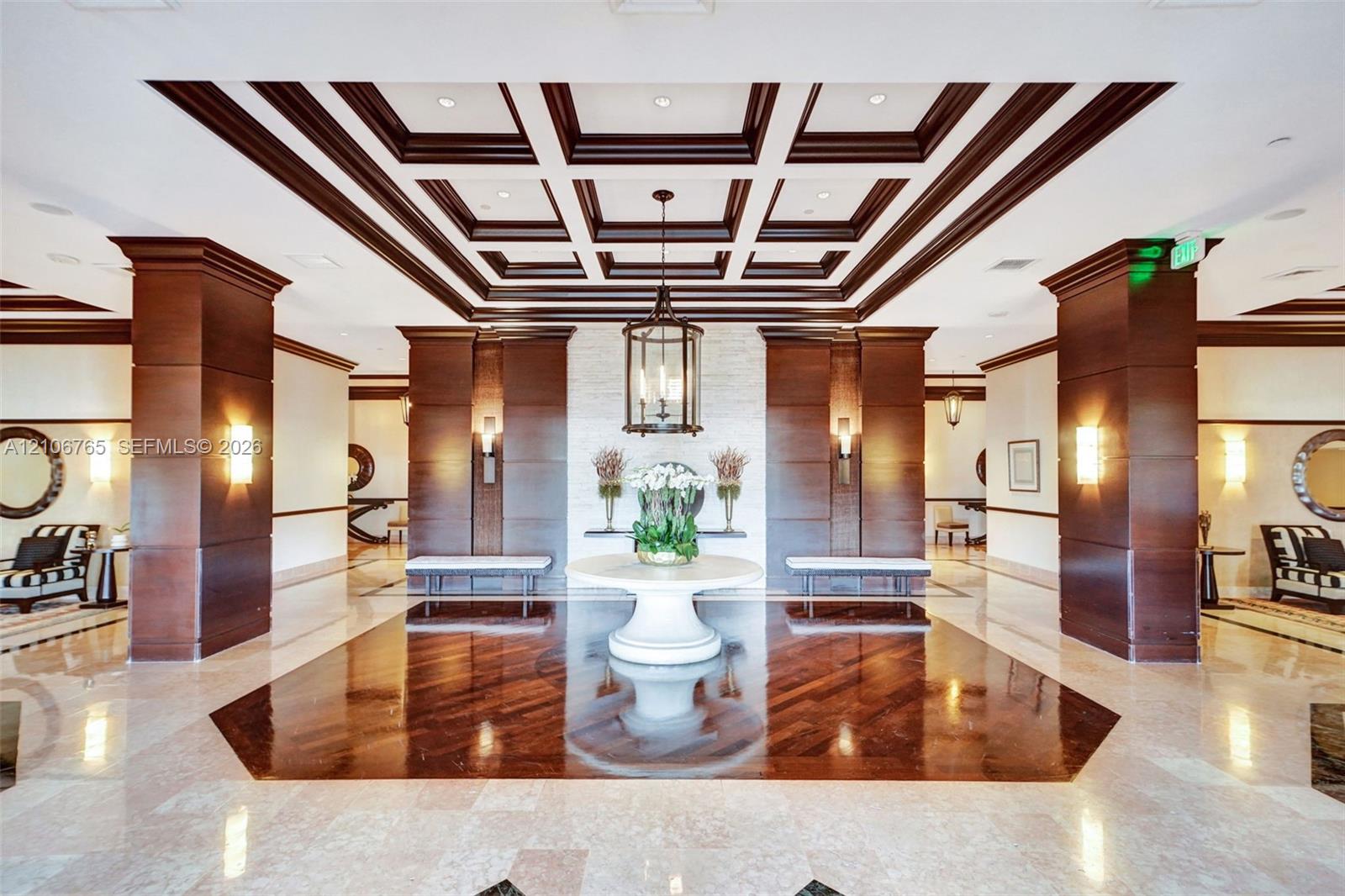 Grand entrance hall, offered ceiling with wood detailing, natural stone flooring with a dark wood-finish inlay, large wood-panelled columns, custom hanging lantern lighting, and a stacked stone accent wall.
