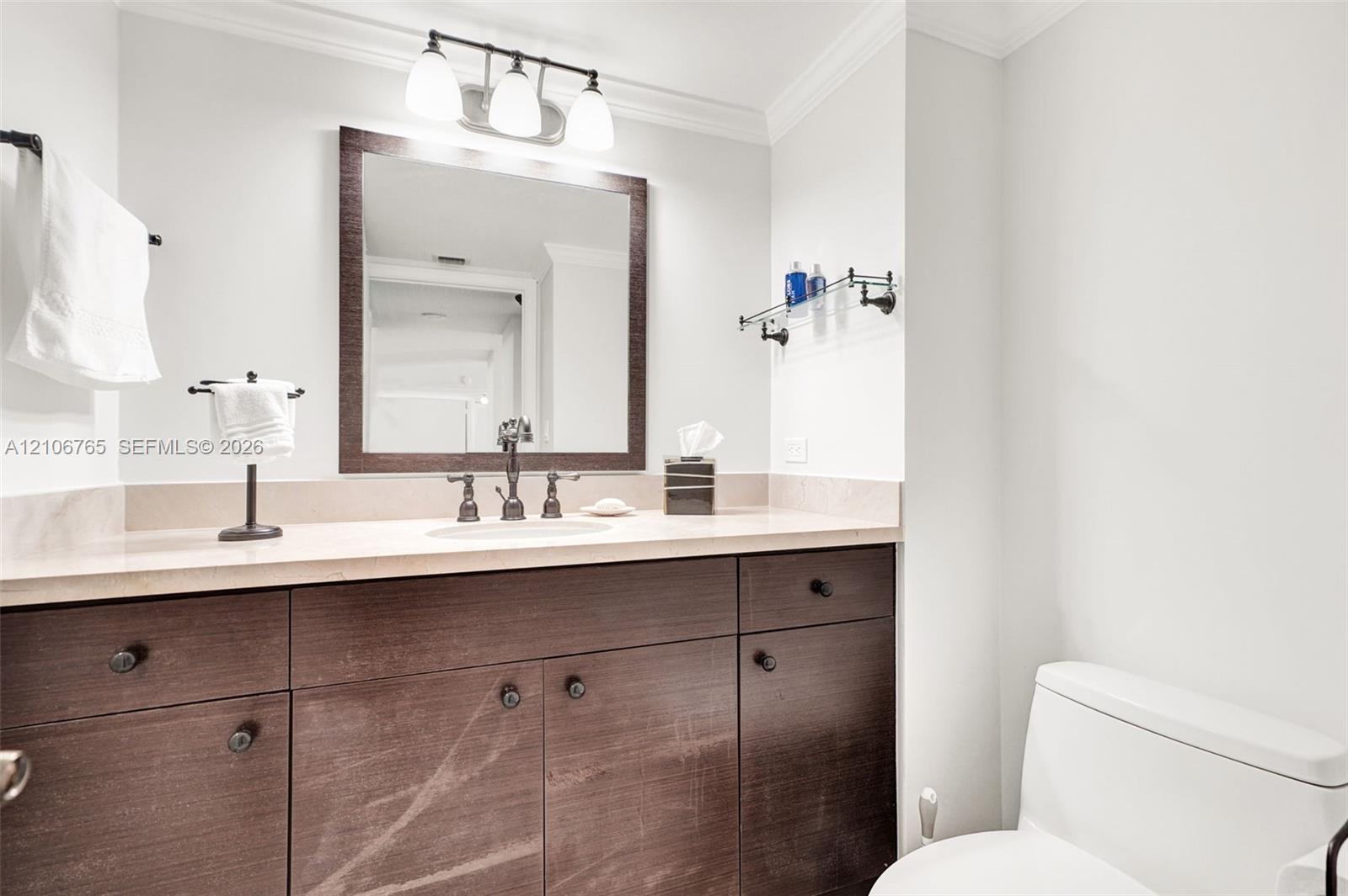 Second bathroom, dark wood-finish cabinetry, light-toned stone countertop, integrated undermount sink, oil-rubbed bronze faucet, three-light vanity fixture, and rectangular framed mirror.